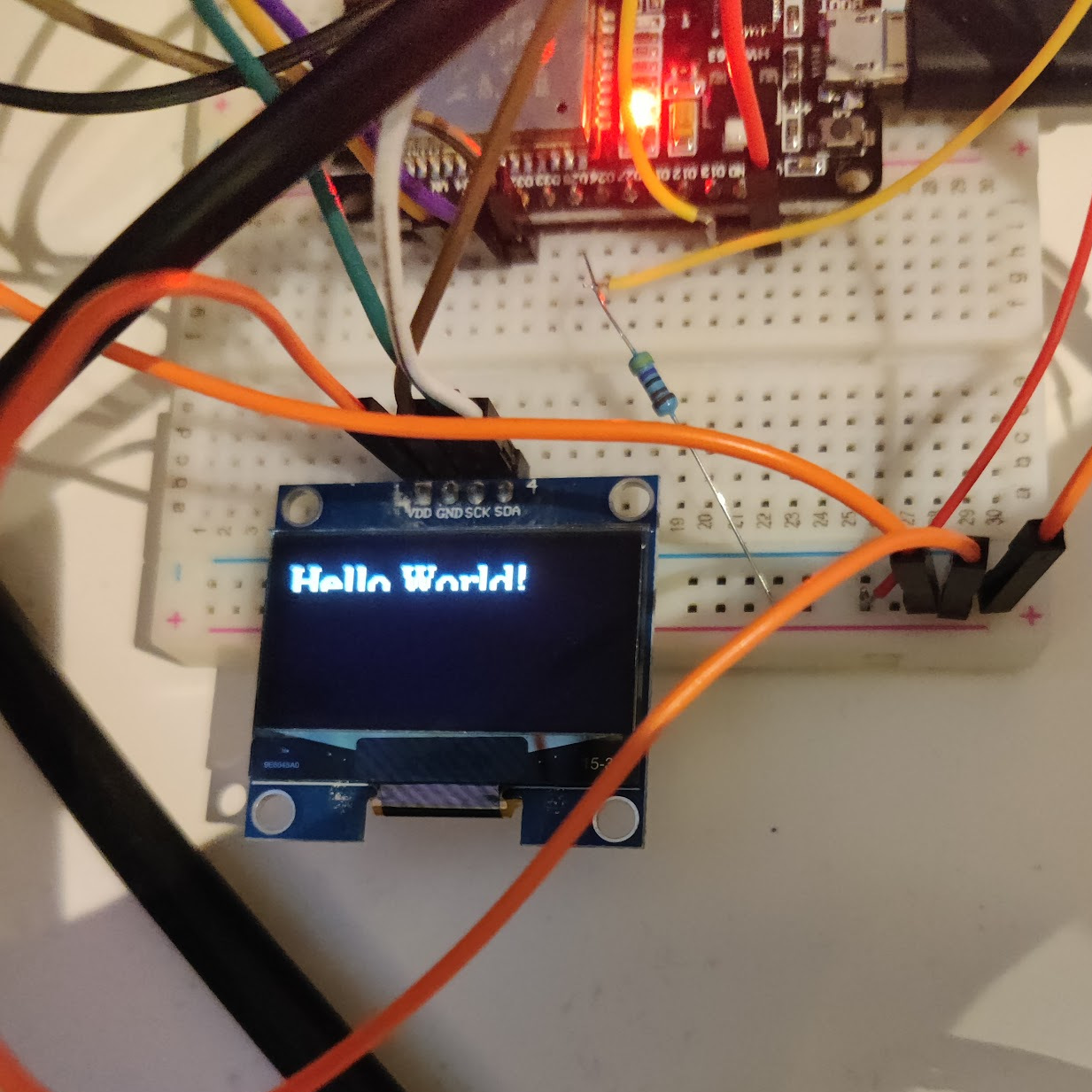A picture of a small OLED screen connected with wires displaying text "Hello World" partially