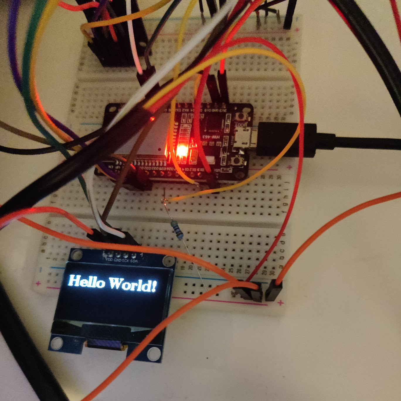 A picture of a small OLED screen connected with wires displaying text "Hello World" completely